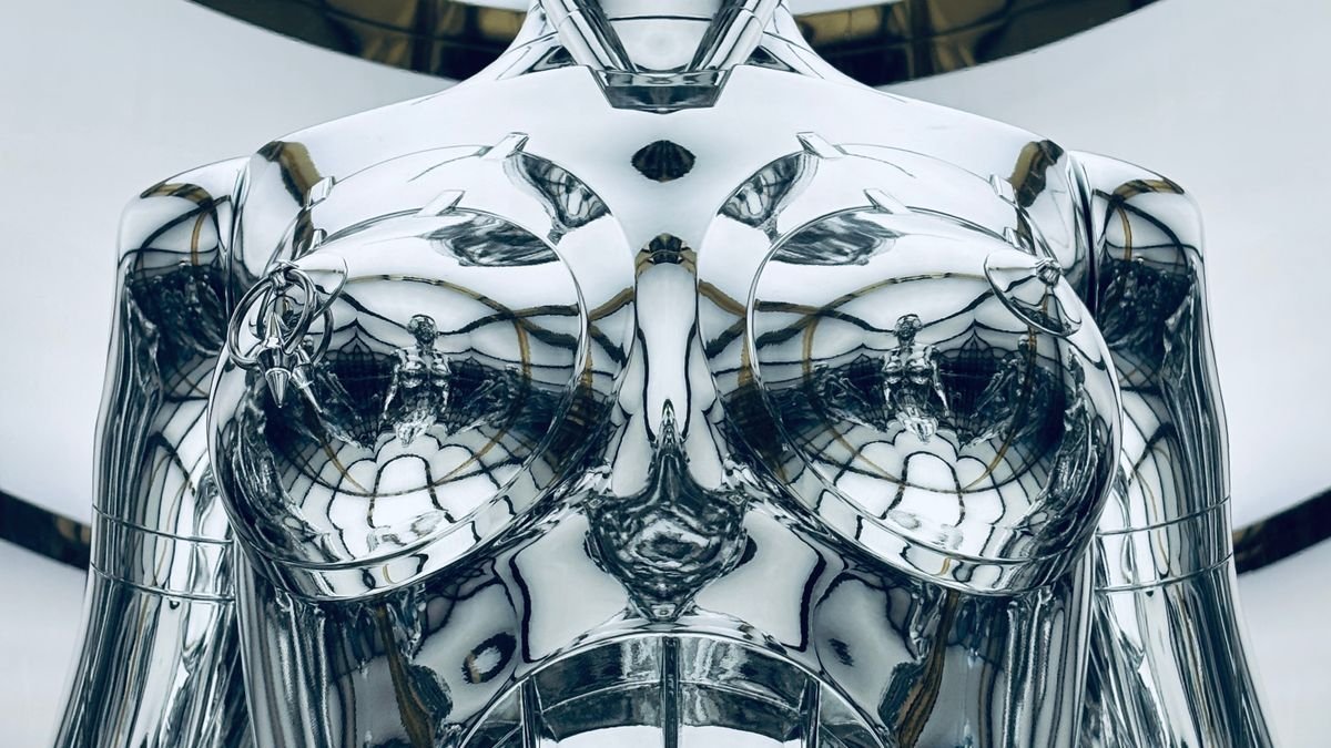 Metalik gorunumlu bir robot heykelinin modern galeri ortaminda sergilenmesi